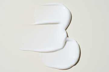 Texture of white cream on beige background. Smear of moisturizer close up. Lotion swatch. Beauty...