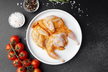 Marinated quail on white plate with fresh tomatoes, salt and spices on black background