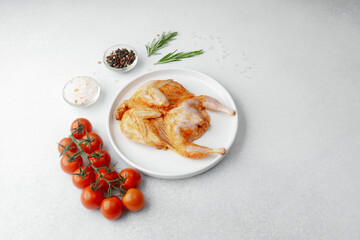 Raw marinated quail on white plate with tomatoes, salt, pepper and rosemary