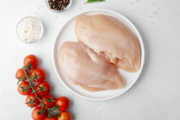 Raw chicken breast on white plate with salt, pepper, rosemary and cherry tomatoes