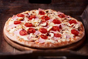 Pizza with ham, cherry tomatoes and mozzarella cheese. Wooden background. Soft focus. Close up.	