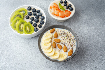 Variety of oatmeal bowls with fruits nuts and chia seeds on gray table