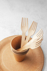 Eco paper cups with wooden forks on disposable plate on white background
