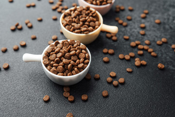 Close view of colorful bowls with dry dog food and scattered kibbles on black background
