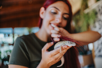 A cheerful girl with long hair gently plays with a leopard gecko indoors, highlighting a playful...
