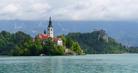 Beautiful island church in Lake Bled, surrounded by nature under soft cloud sky in Slovenia
