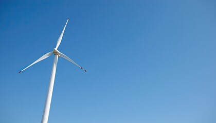 a wind turbine standing tall on the left side of the frame, set against a clear blue sky, the right side of the image is left empty for text or graphics.