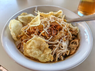 Traditional Indonesian chicken noodle dish with crackers served in a white bowl