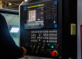 Hand operates CNC machine control panel in factory setting. Close-up view of screen, buttons, and dials for manufacturing automation and precision engineering, highlighting modern industrial technolog