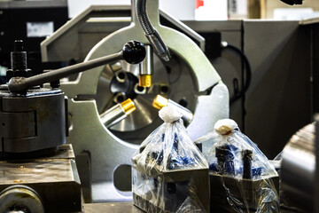 Close-up of metalworking machine parts, including a chuck holding metal pieces, a handle, and components wrapped in plastic in a workshop environment.