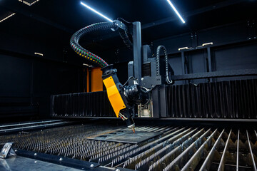 Automated laser cutting machine head processing metal plate in a dark industrial workshop. Precision manufacturing technology.