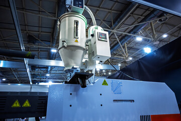 Close-up view of industrial plastic processing machinery in a factory setting, showing hopper, control unit, warning symbols, and technical details.