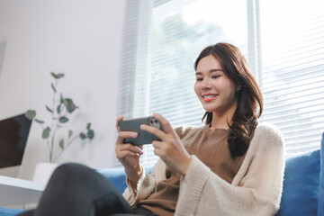 Obraz premium Young woman relaxing on sofa using smartphone at home