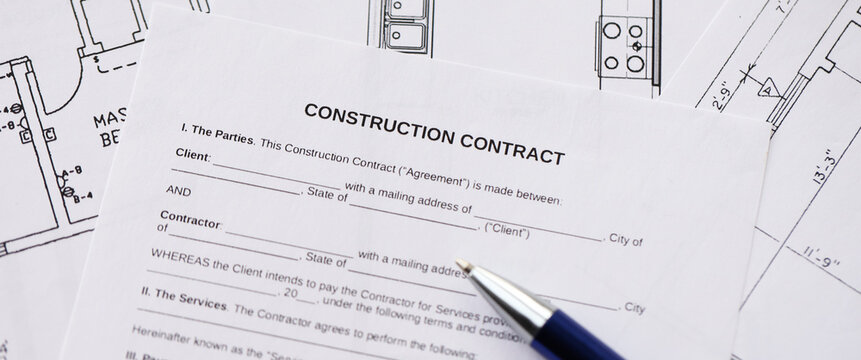 Pen on residential construction agreement and planning blueprints of residential building project