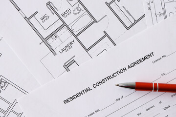 Pen on residential construction agreement and planning blueprints of residential building project