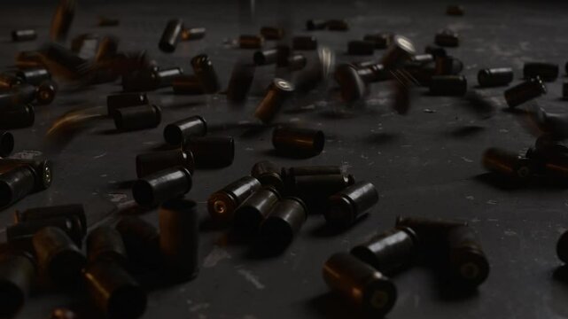Stab close up no people shot of dozens of brass shell casings falling, bouncing and scattering across dark floor at indoor shooting range after rapid fire