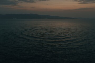 Gentle ripples spread across a calm lake at dusk, with mountains silhouetted in the distance under a twilight sky.