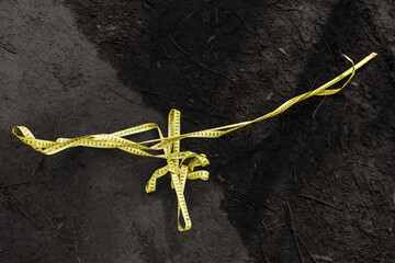 Tangled yellow measuring tape lies on dark soil, symbol of construction or garden work