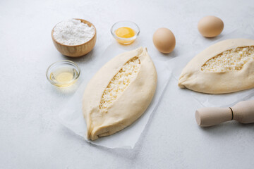 Khachapuri with cheese and baking tools on white kitchen surface