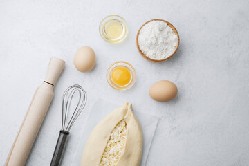 Raw khachapuri with egg yolk and cheese on white background with ingredients
