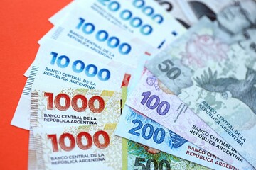 Argentine pesos money bills in big amount lies on red color table close up