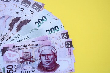 Mexican pesos money bills in big amount lies on yellow color table close up