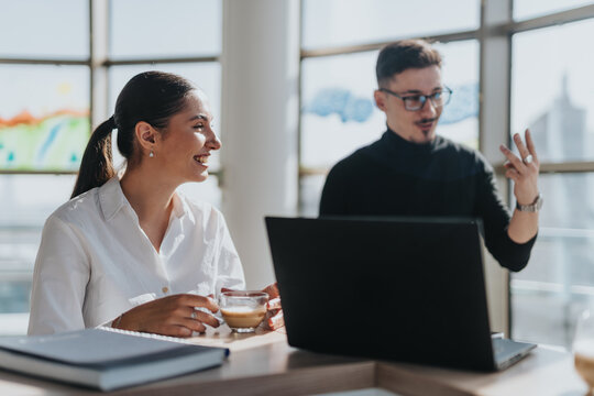 Two business employees engage in a lively discussion in a bright and modern office kitchen, creating a collaborative work atmosphere.