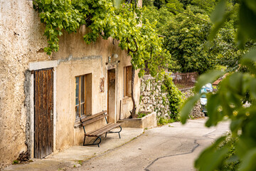 Rustic Street Scene In Vipava, Slovenia: Old Stone House With Wooden Doors And A Bench Beneath...