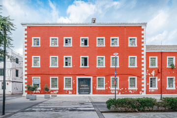 Striking Red Building With White Trim And Multiple Windows In A Menorcan Town. Mediterranean Architecture, Vibrant Facade, Spanish Island Life, Urban Scene