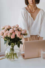 Elegant woman working with laptop and pink roses on desk. Aesthetic minimalist home office workspace