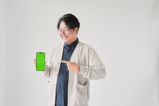 A man is holding a green phone and pointing to it. He is smiling. The phone is green and has a green screen