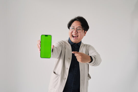 A man is holding a green phone and pointing to it. He is smiling. The phone is green and has a green screen