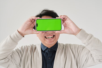 A man is holding a phone with a green screen. He is smiling and looking at the camera