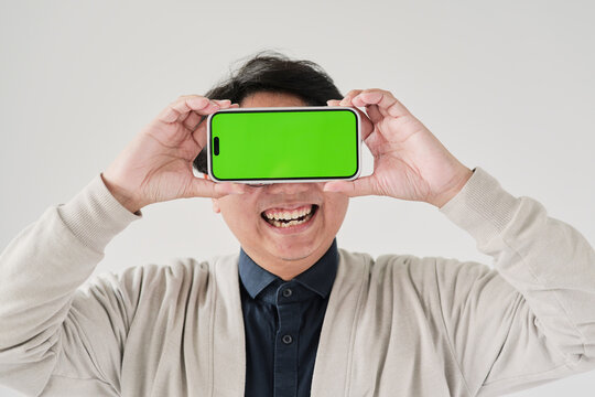 A man is holding a phone with a green screen. He is smiling and looking at the camera