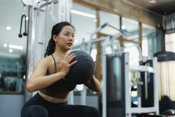 Fototapeta premium Asian woman performing squats with medicine ball in gym