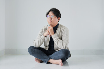 A man is sitting on the floor with his hands clasped in front of him