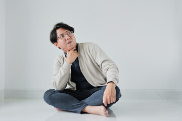 A man is sitting on the floor with his hands on his chin