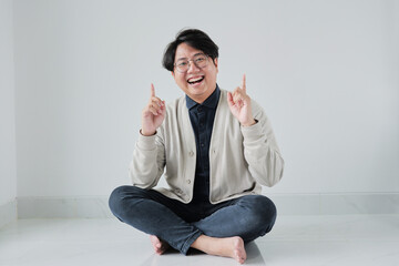 A man is sitting on the floor with his arms raised and pointing to the sky