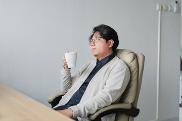 A man is sitting in a chair with a white cup in his hand
