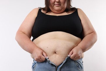 Overweight woman trying to put on tight jeans against white background, closeup