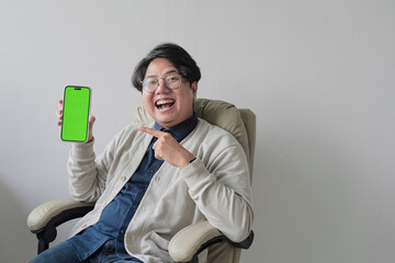 A man is sitting in a chair and holding a green phone
