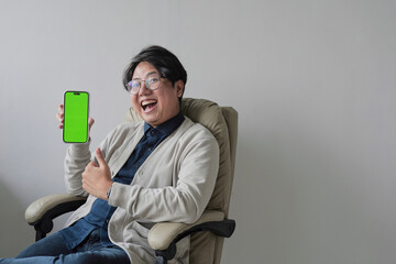 A man is sitting in a chair holding a green phone