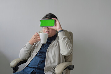 A man is sitting in a chair with a green screen on his phone
