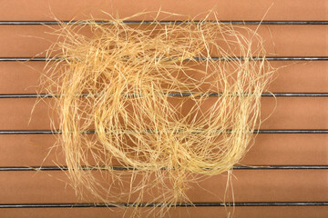 A tangled pile of light-colored corn silk rests on a metal grill over a brown background, viewed...