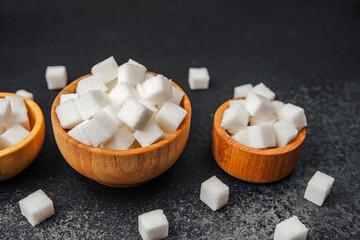 Cubes of sugar scattered in wooden bowls on a dark surface