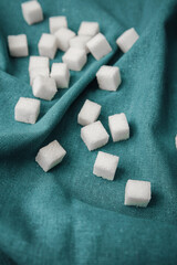 Cubes of sugar scattered on a teal fabric background in a cozy setting