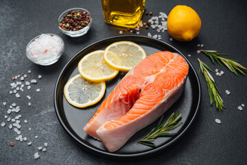 Fresh salmon fillet with lemon and spices arranged on a black plate