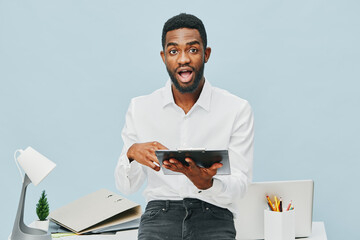 Enthusiastic young man with dark skin and curly hair, dressed in a white shirt, holding a digital...