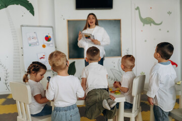 Obraz premium Female is standing and showing picture of puzzle. Children in kindergarten with their teacher