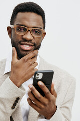 Stylish young African American man wearing glasses and a beige blazer holding a smartphone,...